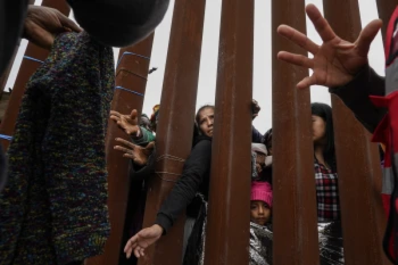 migrants-reach-through-a-border-wall-for-clothing-handed-out-by-volunteers-as-they-wait-between-two-border-walls-to-apply-for-asylum-friday-may-12-2023-in-san-diego-2a40df43975bb753e31d59a990ef06211715061082.png
