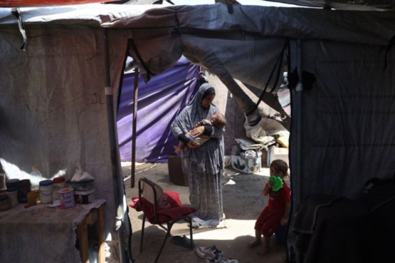 madeline-a-mother-from-gaza-stands-in-her-tent-holding-her-child-in-her-arms-baab3331b9678d6f187752f1838a4e541729707298.jpg